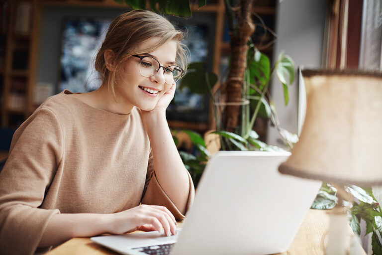 Cheerful Young Caucasian Girl In Glasses Using Laptop, Shopping